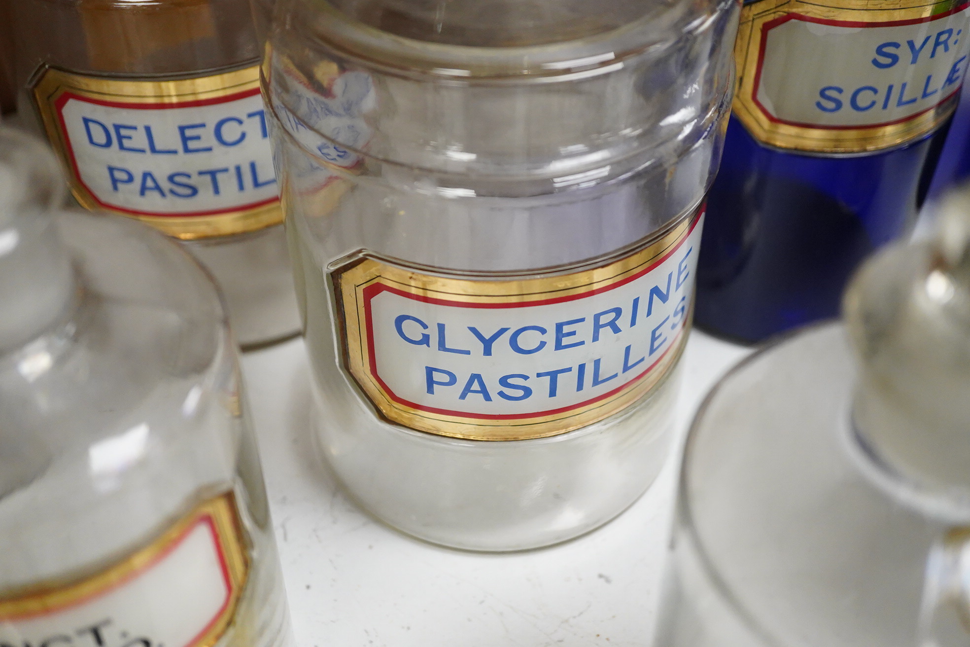 Seventeen 19th/early 20th century glass apothecary jars with gilt rimmed labels; six blue glass, ten clear glass and a green glass example, labels including; Syr: Zingib:, Chloroform, Syr: Rhei:, Camphora, etc. tallest 2